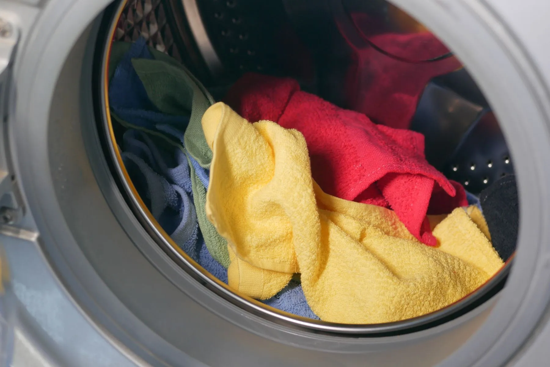 Yellow, red, blue and green towels inside the drum of a front-loading washing machine